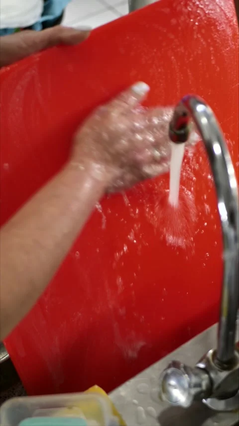 Washing a cutting board with bare hands in a sink with soap and water while Stock Footage 306318703