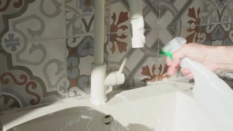 Washing green cloth under running kitchen faucet against patterned ceramic Stock Footage 346152161