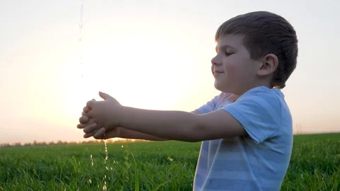 Washing hands of tiny boy and water splash in green field on background sky in 스톡 동영상 85385582