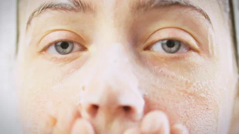 Washing her face with fluffy white cleansing foam girl stands in bright bath Stock Footage 346393368