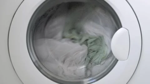 Washing machine drum filled with white and light green laundry, water and Stock Footage 334691184