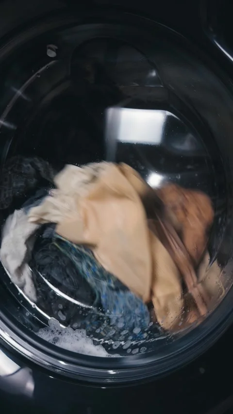 Washing machine drum spinning, cleaning colorful and white clothes, creating a Stock Footage 344911495