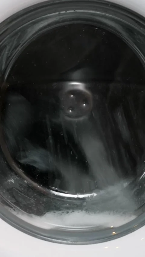 Washing machine drum spinning clothes with soapy water during laundry cycle Stock Footage 341678151
