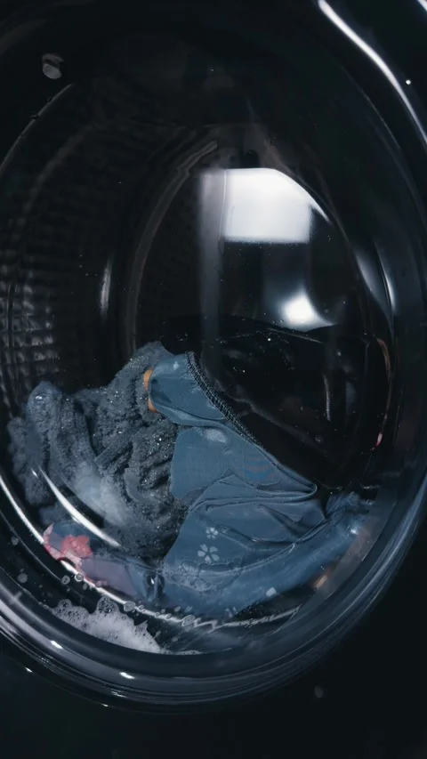 Washing machine drum spinning clothes during laundry cycle, showcasing domestic Vídeo Stock 344911440