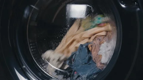 Washing machine drum spinning with colorful clothes and water during laundry Stock Footage 344911971