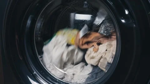 Washing machine drum spinning with colorful clothes, water, and detergent foam Stock Footage 344912170
