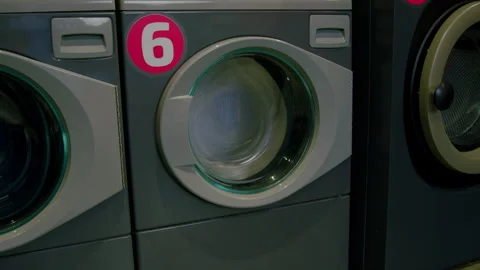 Washing machine in laundromat showing continuous motion of spinning clothes Video stock 330015738