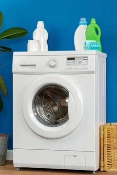 Washing machine with laundry detergent on a blue wall in a home setting Stock Photos