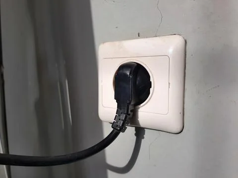 A washing machine plug is being connected to the power outlet socket on the wall Stock Photos