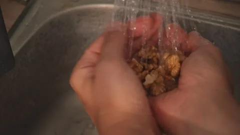 Washing walnuts under running water in kitchen sink Stock Footage 312708535