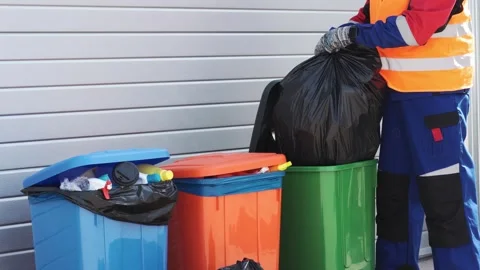 Waste collection worker sorts trash at local facility in vibrant recycling bins Stock Footage 299684151