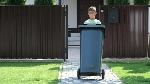 Waste collector garbage removal from a private house. boy rolls out trash can 库存影片 280392634