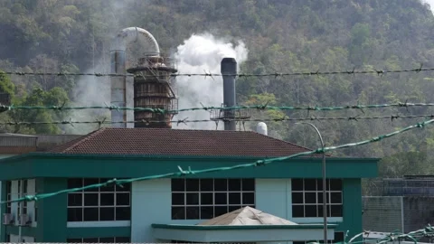 A waste processing factory operates in the tropical heat, its smokestacks 스톡 동영상 314664954