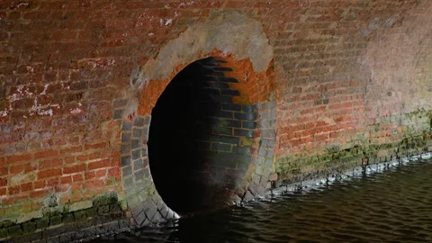 Wastewater drainage outlet in old brick wall beside waterway. Sewer discharge Vídeo Stock 346037586