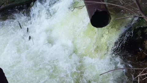 Wastewater flows from a pipe into a river, creating turbulent waves Stock Footage 304790509