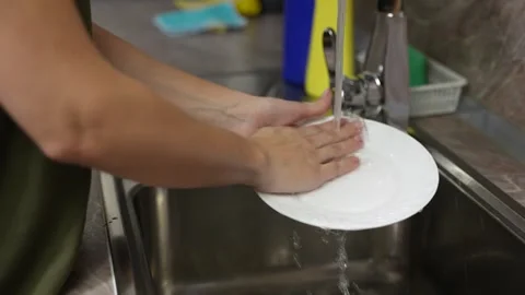 Watch closely as a woman's hands gently scrub a white plate under the running Видео 257206776