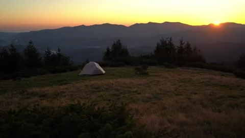 Watch the sunset over the mountains while camping in a tent on a hillside Stock Footage 327445809