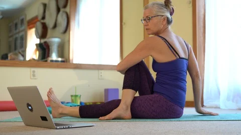 Watching a computer laptop screen, a mature woman stretches doing a yoga pose Stock Footage 128639155