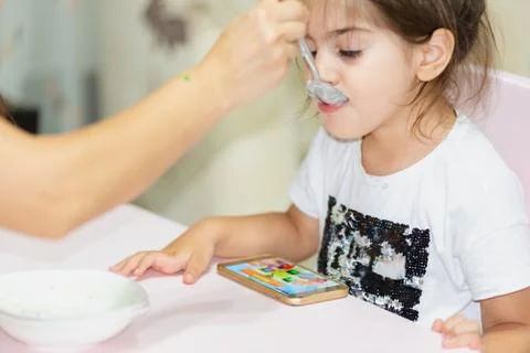 Watching smart phone while feeding girl Stock Photos