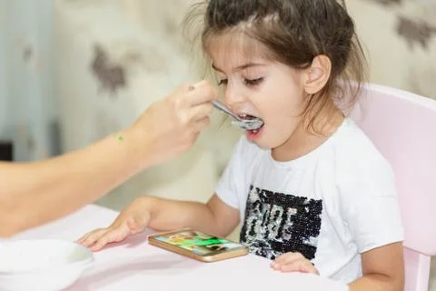 Watching smart phone while feeding girl Stock Photos