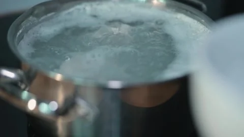 Water is boiling in a pot on a stove as another ingredient is prepared. This Stock-Footage 338301339