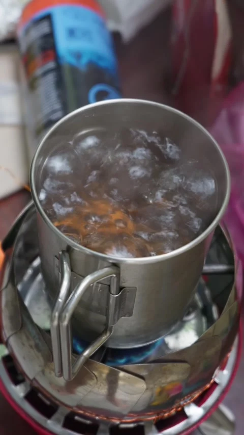 Water Boiling Rapidly Inside Metal Mug Sitting on Camping Gas Stove 库存影片 341995769