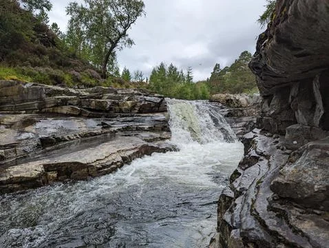 Water cascade on small rock cliffs with trees and a cloudy sky in the background 스톡 사진