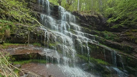 Water cascades down mossy, layered rocks. Slowmotion. Tupavica Waterfall Stock Footage 335536120