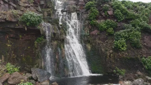 Water cascades down rocky cliffs with green foliage Vidéo 342926712
