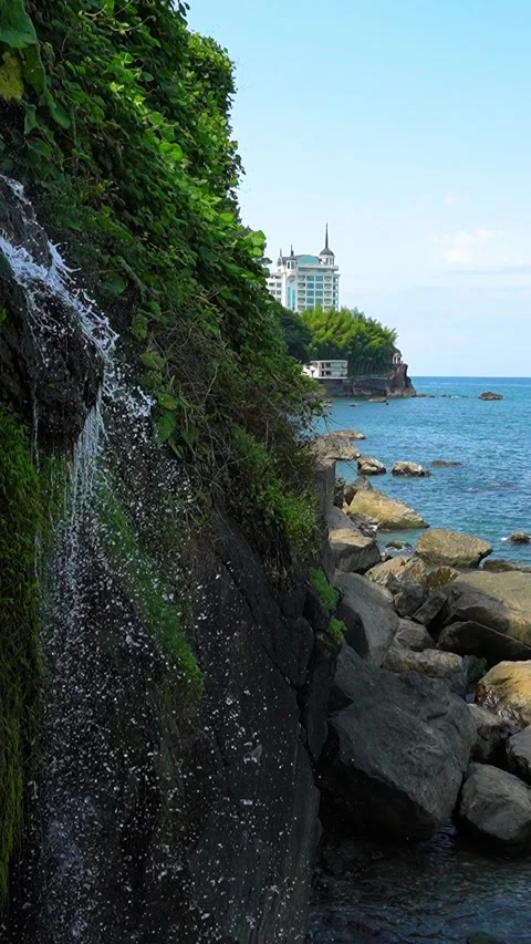 Water cascading down lush cliffside by the ocean Stock Footage 283362189