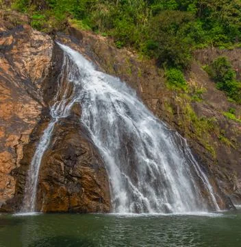 Water cascading down rocky cliffs into a pool in Goa Stock Photos