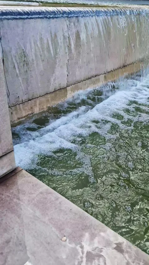 Water Cascading Down Textured Stone Wall Into Modern Garden Fountain Pool Stock-Footage 339077931