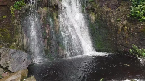 Water crashes over mossy rocks into dark pool below Vidéo 342929036