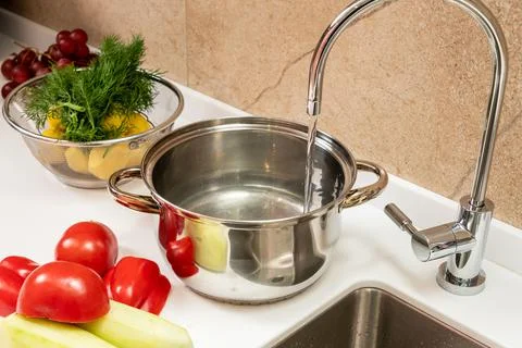 Water is drawn into a pot on the table next to the sink and cooked vegetables Stock Photos
