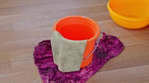Water dripping from ceiling leak into an orange plastic bucket on wooden floor Stock Footage 331186957