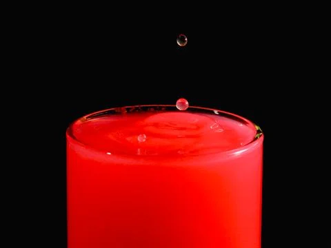 A water drop creating a splash in a red-colored liquid. Foto stock