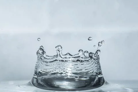Water drop falling and colliding creating tall wave with small droplets on side Stock Photos