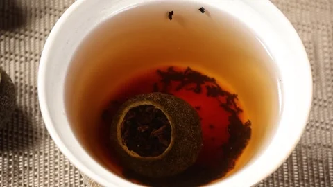 Water drop falling into cup of tangerine Puerh tea slow motion Stock Footage 339424984