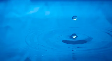 Water drop falling into water Stock Photos