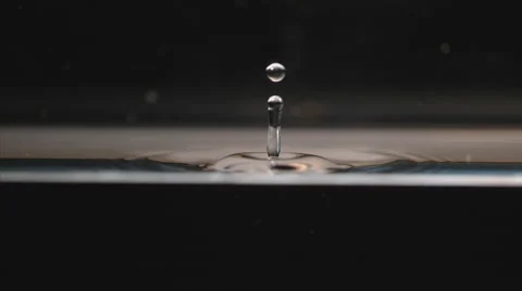 Water drop falls to calm surface, splashing in geometric ripples on black Stock Footage 63832923