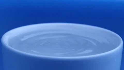 Water drop falls into the filled cup on blue background in slow motion. Stock Footage 142820661