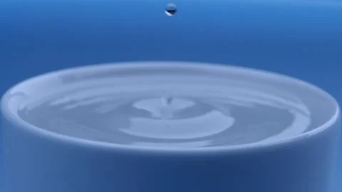 Water drop falls into the filled cup on blue background in slow motion. Stock Footage 142884928