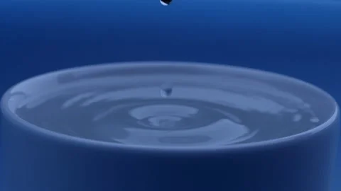 Water drop falls into the filled cup on blue background in slow motion. Stock Footage 142884929