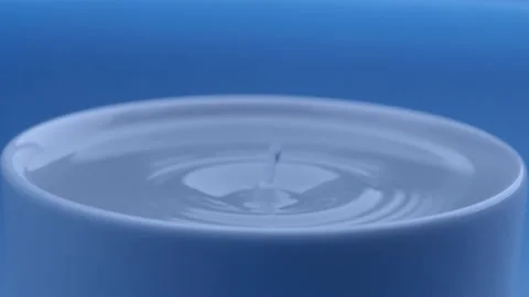 Water drop falls into the filled cup on blue background in slow motion. Stock Footage 142884970