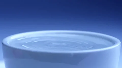Water drop falls into the filled cup on blue background in slow motion. Stock Footage 143254712