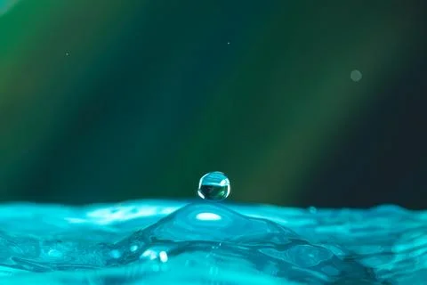 Water droplets fall down closely into the blue water, making it the perfect c Stock Photos