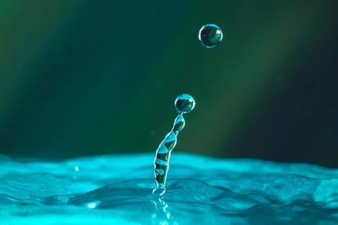 Water droplets fall down closely into the dark blue water, making it the perf Stock Photos