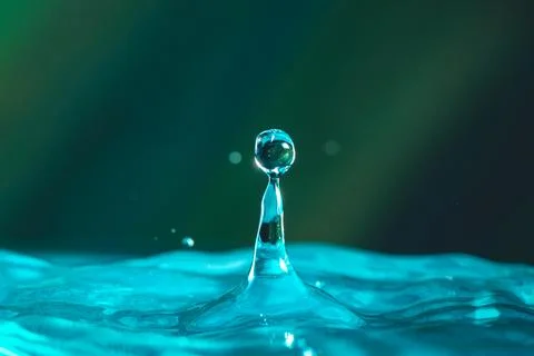 Water droplets fall down closely into the dark blue water, making it the perf Stock Photos