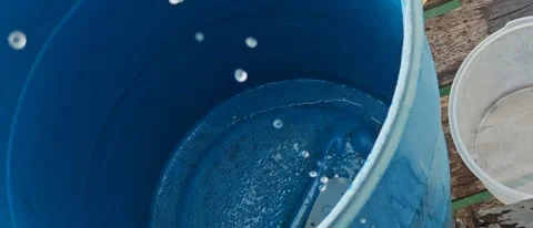 Water droplets falling and splashing inside a large blue plastic barrel. Video stock 336227087