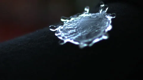Water droplets hit black object and explode in all directions. ECU. Slow motion. Stock Footage 64871017